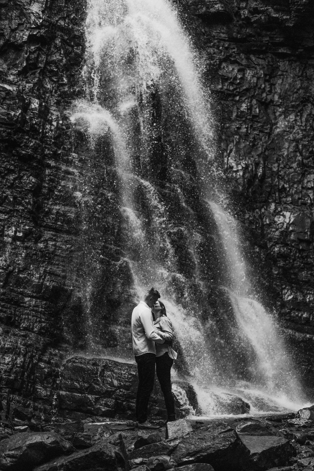 Black and White Photo of Couple Kissing under Waterfall
